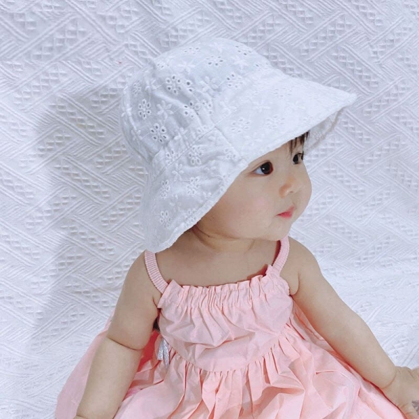 Kleine Asiatin sitzt mit einem rosa Kleid und einer weißen Baskenmütze und schaut nach rechts
