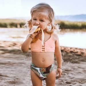 Zweiteiliges Badeanzugset für Mädchen, das von einem kleinen Mädchen am Strand getragen wird.