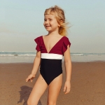 Lächelndes blondes Mädchen am Strand mit einem einteiligen Badeanzug