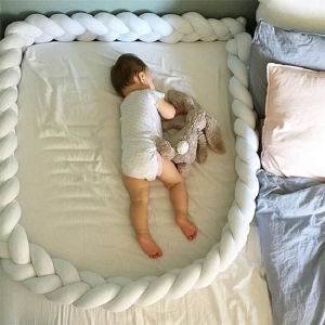 Schutzbettumrandung für eine Mädchenwiege auf einem Bett mit einem Baby im Inneren in einem Haus
