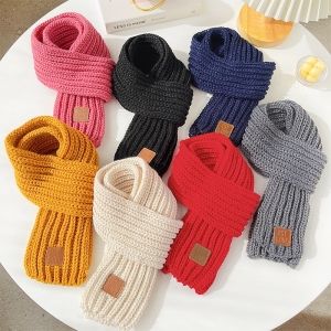 sieben geknüpfte Schals, die auf einem runden weißen Tisch liegen, die Farben sind rosa, schwarz, dunkelblau, gelb, weiß, rot, grau auf einem weißen Tisch