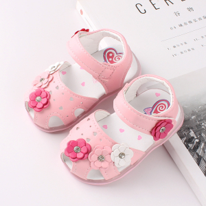 Rosafarbene Sandale für Mädchen mit 4 kleinen Blumen in verschiedenen Farben, die auf einer Zeitschrift und einem weißen Tisch steht