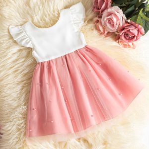 Weißes und rosafarbenes Tüllkleid mit kurzen Ärmeln und Rüschen für ein Mädchen, das flach auf einem langflorigen Teppich neben gleichfarbigen Rosen präsentiert wird