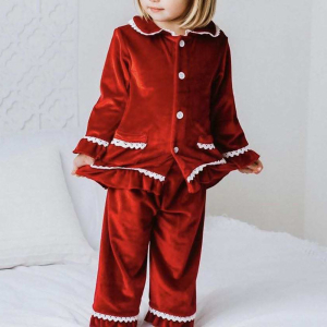 Kleines blondes Mädchen, das in einem Weihnachtspyjama aus rotem Samt steht