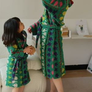 Braunes Mädchen mit einer erwachsenen Person in einem Raum, beide tragen einen grünen Bademantel mit Gemüsemuster