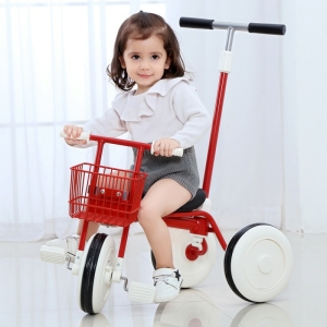 Kleines braunes Mädchen sitzt auf einem roten Dreirad in einem Zimmer am Fenster
