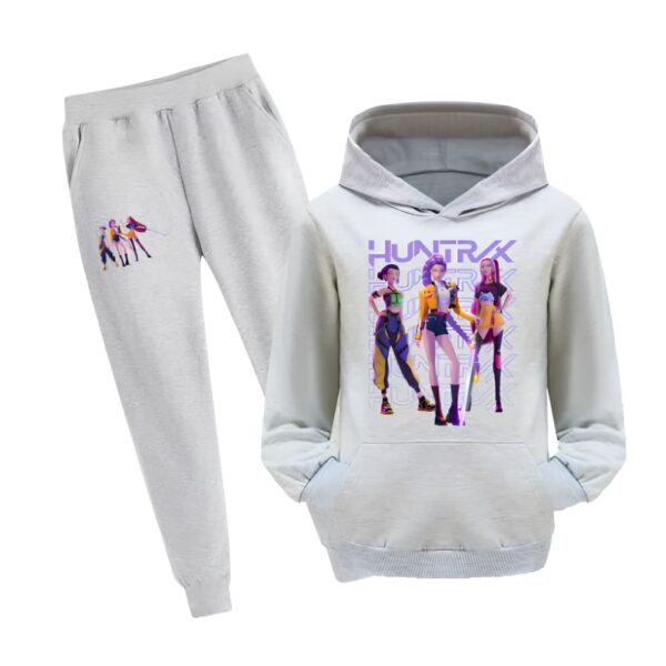 K-pop Demon Hunters Jogginganzug Mädchen mit Sweatshirt mit Kapuze. Das Set ist grau mit einem Motiv auf dem Oberschenkel der Hose und einem großen Motiv mit den drei Heldinnen des Films auf der Vorderseite des Sweatshirts. Das Sweatshirt hat eine Känguru-Tasche. Auf weißem Hintergrund.