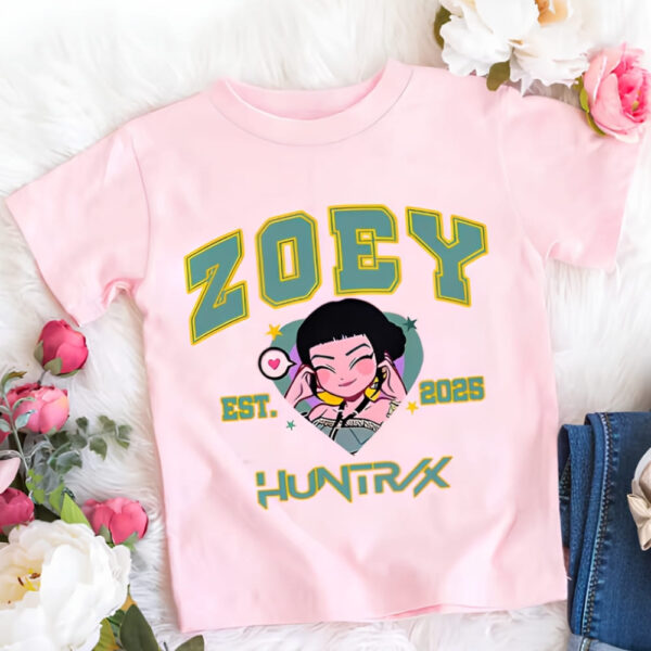 IMG_10_2025_T_shirt_fille_K_pop_Demon_Hunters_rose_du_personnage_Zoey_1.jpg T-shirt fille K-pop Demon Hunters rose du personnage Zoey. Son prénom est écrit en majuscules vertes ainsi que Huntrix sous le portrait de Zoey en version cartoon. Le t-shirt est posé à côté de fleurs.